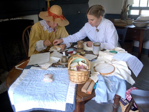 2 women in 19th century clothing, sewing